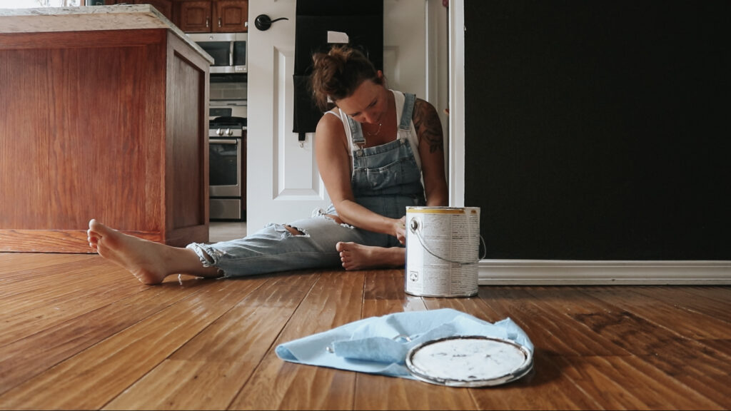 Christian homemaker wearing overalls and white tank top is painting the trim in her house